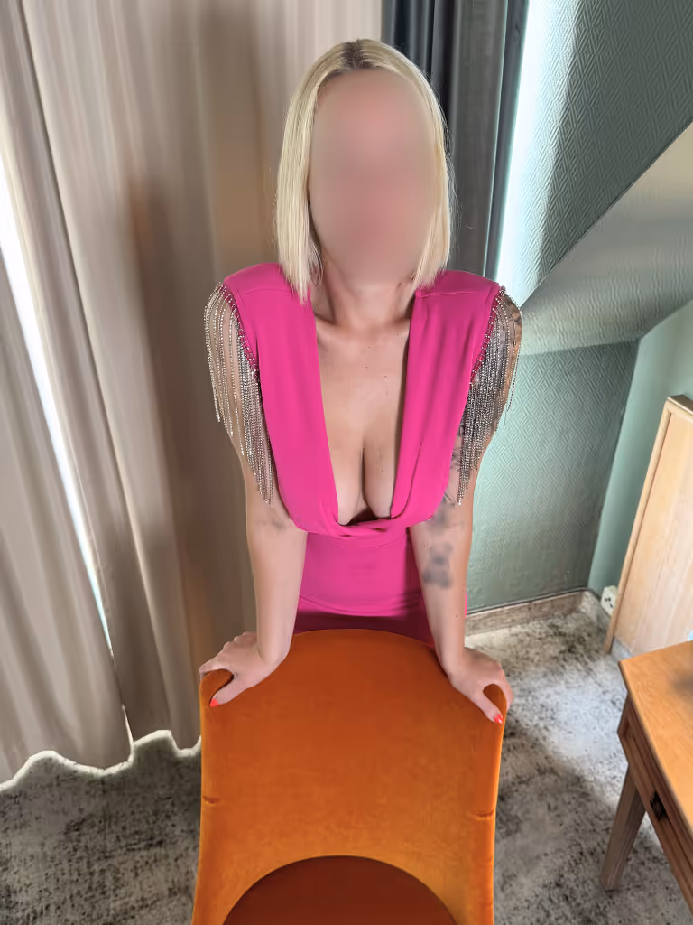 Emilia Escort Hannover in pinkem Dessous, lasziv am Fenster – bereit für aufregende Fantasien.