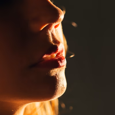 Ein Frauengesicht gegen das Licht fotografiert, die Lippen so geformt, als würden sie etwas verruchtes sagen